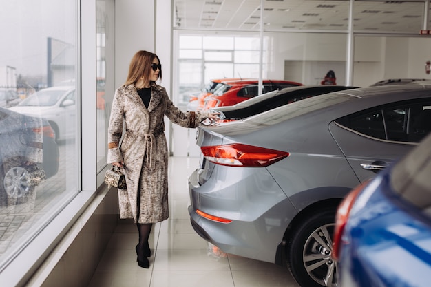 Una giovane donna alla moda sta scegliendo una nuova auto in un negozio di auto