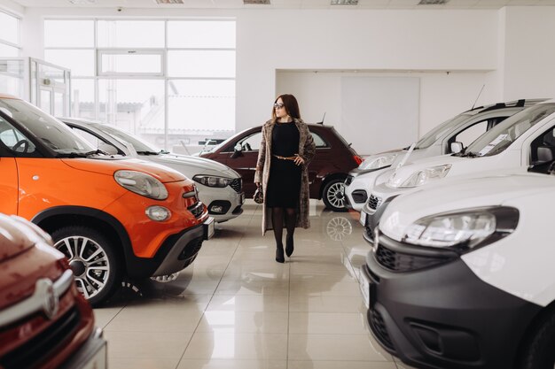 Una giovane donna alla moda sta scegliendo una nuova auto in un negozio di auto