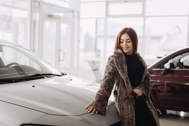 Una giovane donna alla moda sta scegliendo una nuova auto in un negozio di auto