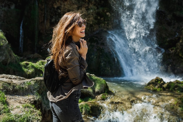 Una giovane donna allegra che si gode la vista della bellissima cascata.