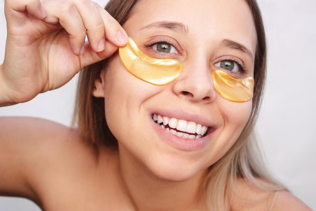 Una giovane donna allegra sorridente piuttosto caucasica mette macchie d'oro sulla pelle sotto gli occhi