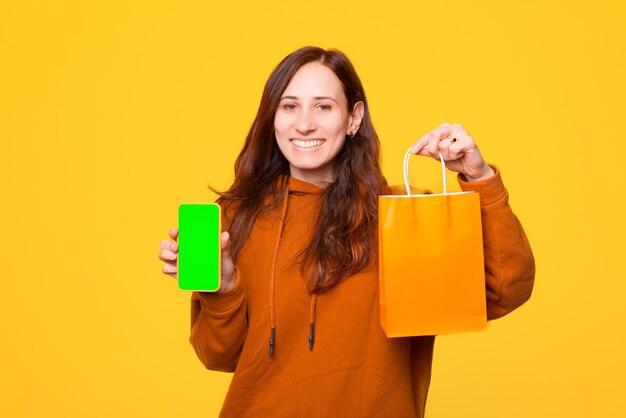 Una giovane donna allegra sta tenendo una borsa della spesa e un telefono