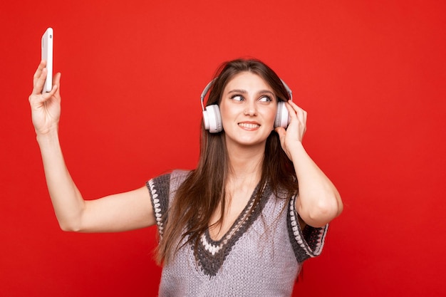 Una giovane donna ascolta la musica con le cuffie e si fa un selfie su uno sfondo rosso