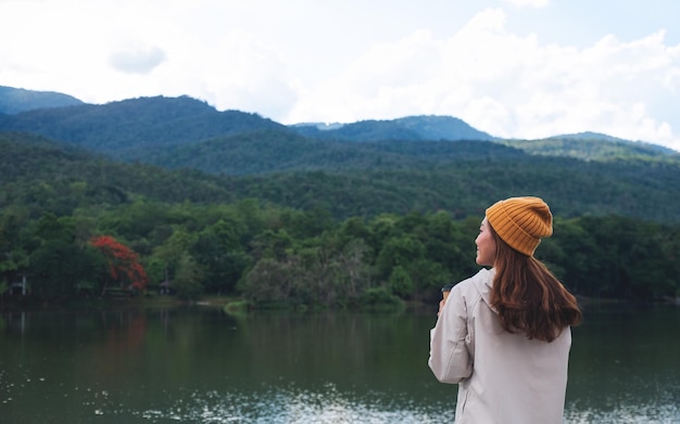 Una giovane donna asiatica che beve caffè mentre viaggia sulle montagne e sul lago