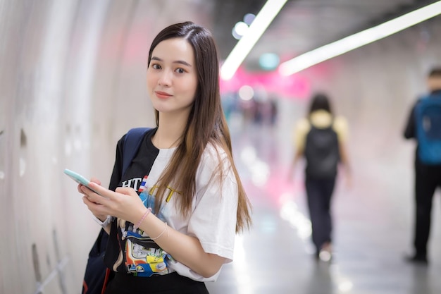 Una giovane donna asiatica che ha i capelli lunghi tiene in mano uno smartphone e si trova nel tunnel della metropolitana