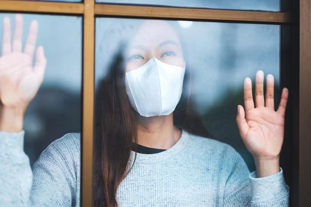 Una giovane donna asiatica che indossa una maschera protettiva mentre resta in isolamento a casa per l'autoquarantena e il concetto di COVID-19