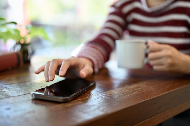 Una giovane donna asiatica che sorseggia un caffè usando il suo smartphone sul tavolo