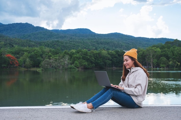 Una giovane donna asiatica che usa e lavora al computer portatile mentre viaggia sulle montagne e sul lago