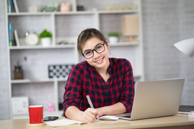 Una giovane donna asiatica con una camicia bianca intelligente indossa un computer portatile mentre è seduta in un ufficio creativo o in ca