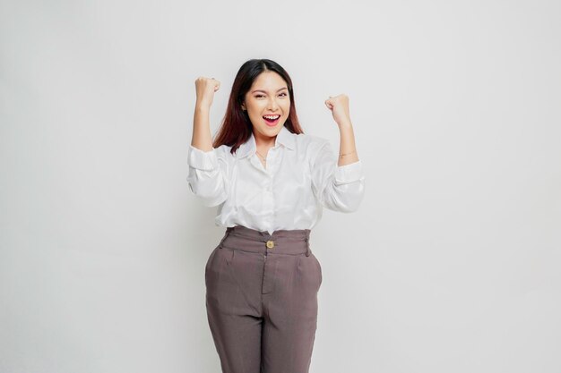 Una giovane donna asiatica con una felice espressione di successo che indossa una camicia bianca isolata da sfondo bianco