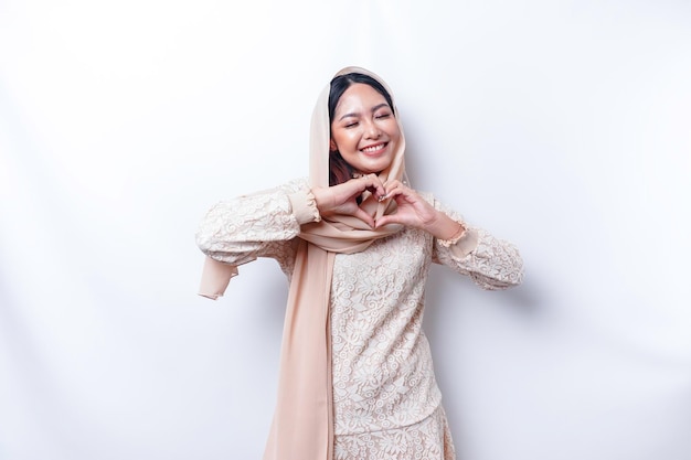 Una giovane donna asiatica felice che indossa l'hijab sente forme romantiche il gesto del cuore esprime sentimenti teneri