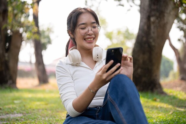 Una giovane donna asiatica felice che usa il suo smartphone mentre si rilassa in un parco verde in una giornata di sole