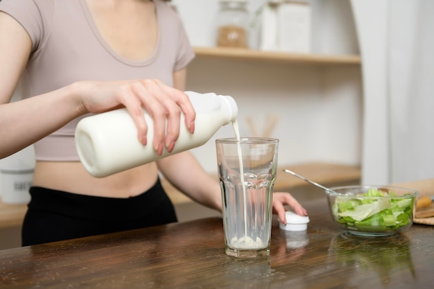 Una giovane donna asiatica in abbigliamento sportivo che beve latte in cucina a casa concetto di stile di vita sano