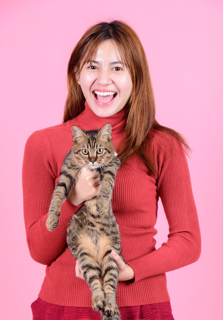 Una giovane donna asiatica piuttosto carina con un maglione rosso tiene un gatto nelle sue mani come un bambino isolato