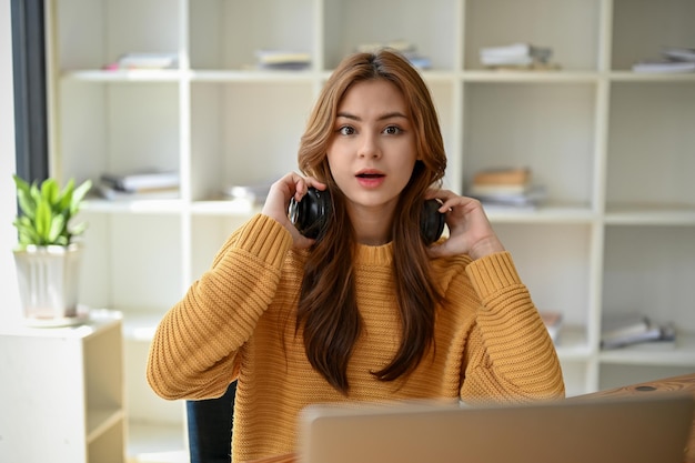 Una giovane donna asiatica scioccata si sta togliendo le cuffie wireless mentre è seduta alla sua scrivania