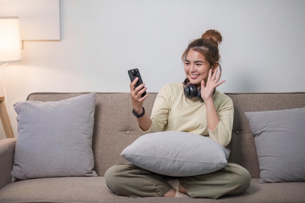 Una giovane donna asiatica sorridente e allegra in abiti casual che si gode di ascoltare musica attraverso le cuffie nella sua stanza di lavoro a casa
