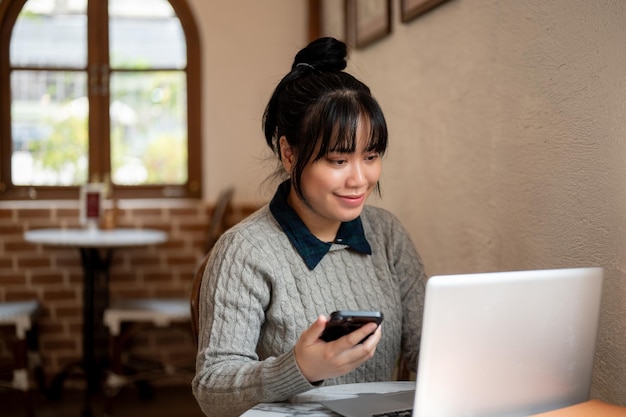 Una giovane donna asiatica sorridente e positiva sta lavorando a distanza in un caffè su il suo portatile