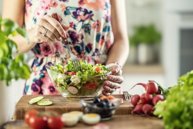 Una giovane donna assaggia una sana insalata con una forchetta nella sua cucina