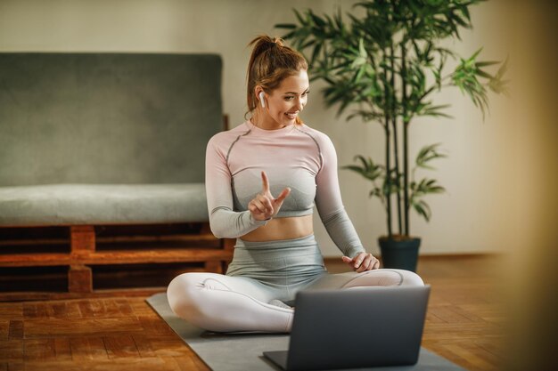 Una giovane donna attraente che usa il laptop per registrare il suo vlog sulla vita sana mentre fa esercizi a casa.