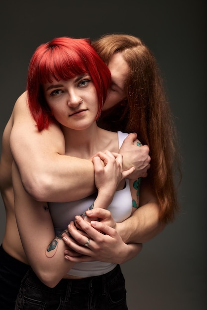 Una giovane donna attraente con i capelli color rubino brillante tra le braccia di un uomo seminato con i capelli lunghi, l'amore