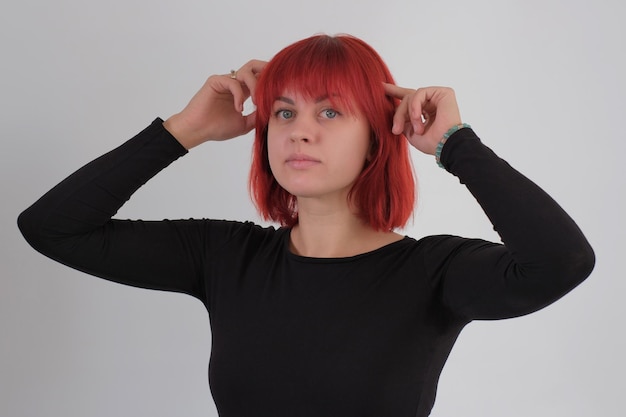 Una giovane donna attraente con un taglio di capelli corto arancione in una maglietta nera e jeans in posa in studio su uno sfondo bianco