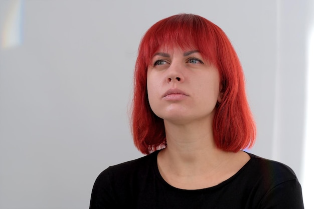 Una giovane donna attraente con un taglio di capelli corto arancione in una maglietta nera e jeans in posa in studio su uno sfondo bianco