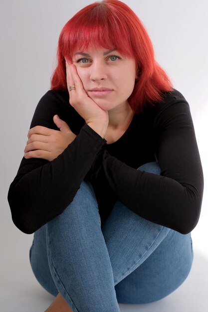 Una giovane donna attraente con un taglio di capelli corto arancione in una maglietta nera e jeans in posa in studio su uno sfondo bianco