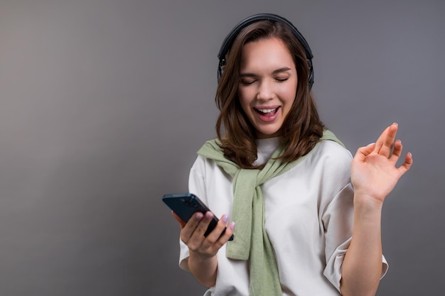 Una giovane donna balla con la musica che ascolti con le cuffie Sfondo grigio isolato