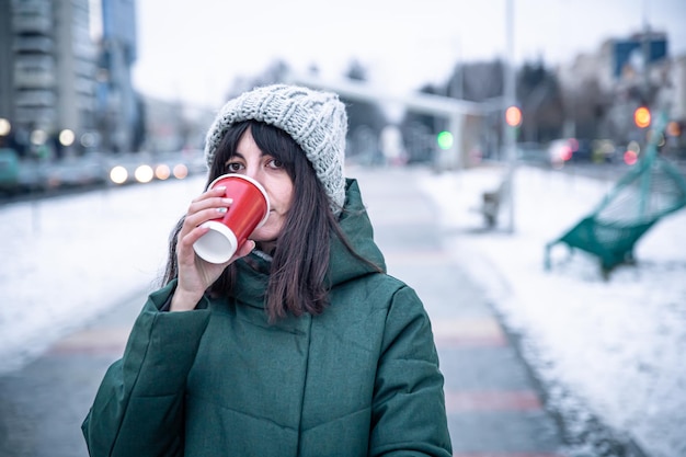 Una giovane donna beve caffè durante una passeggiata in città in inverno