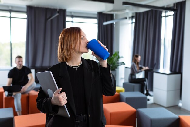 Una giovane donna beve il caffè sullo sfondo di un ufficio di lavoro