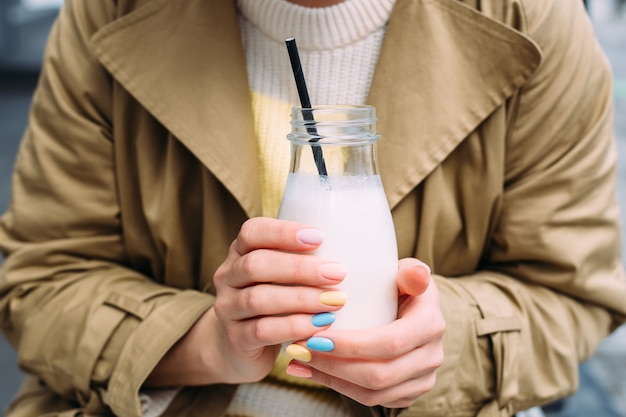 Una giovane donna beve un frullato all'aperto da un elegante barattolo di vetro con una cannuccia