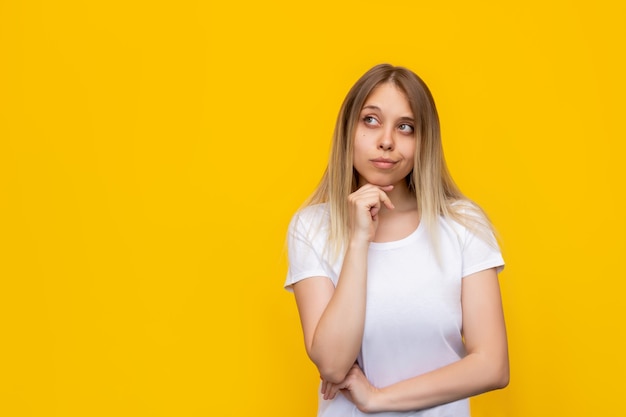 Una giovane donna bionda abbastanza premurosa caucasica in una maglietta bianca immagina pensa distogliere lo sguardo dallo spazio vuoto della copia per annunci promozionali offerta citazione slogan di testo isolato su un muro giallo di colore brillante