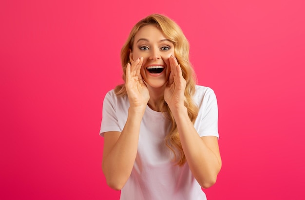 Una giovane donna bionda felice che grida tenendosi per mano vicino alla bocca dello studio