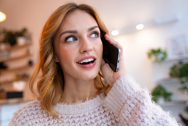 una giovane donna bionda piuttosto ottimista si siede in un caffè al chiuso parlando al telefono cellulare.