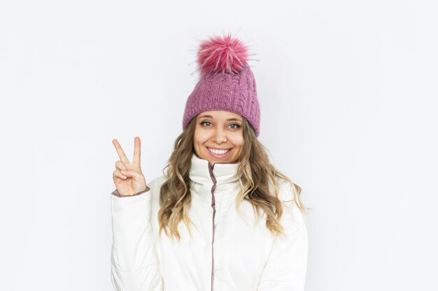 Una giovane donna bionda sorridente felice in un abbigliamento invernale mostra un gesto di pace con la mano
