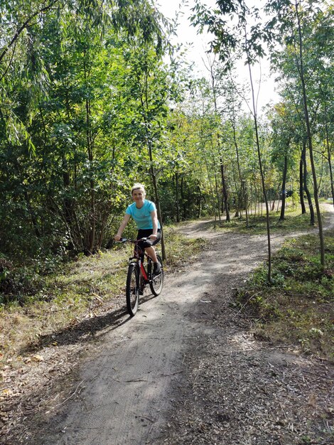 Una giovane donna bionda va in bicicletta lungo un sentiero nella foresta vista anteriore Turismo e sport