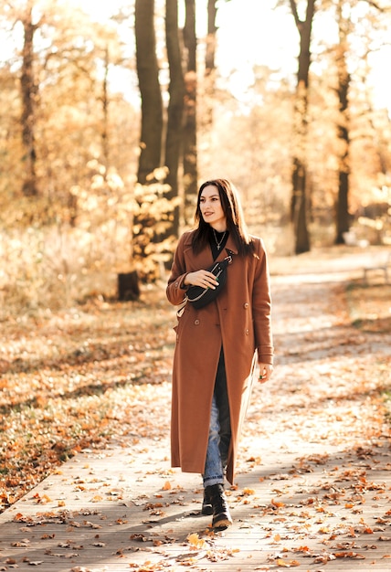 Una giovane donna bruna con un cappotto in autunno cammina nel parco