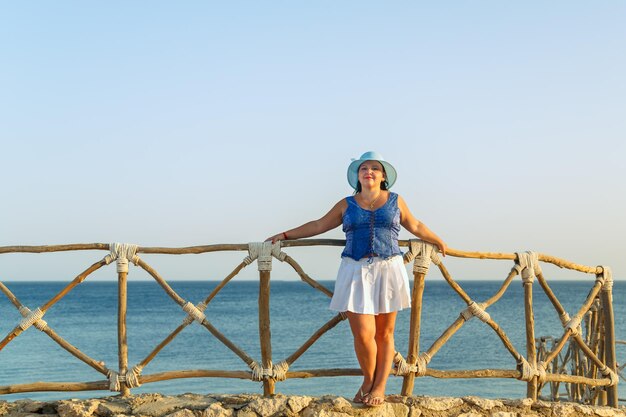 Una giovane donna bruna con una gonna bianca e un cappello da sole in riva al mare si oppone