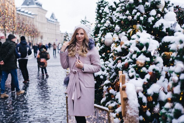 Una giovane donna cammina a Natale nella piazza vicino agli alberi di Natale decorati. Candy è una lecca-lecca a forma di cuore.