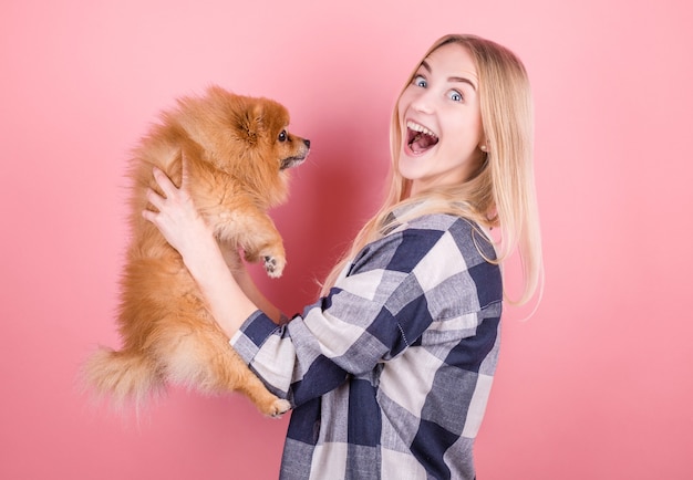 Una giovane donna carina sta tenendo il suo cucciolo di Pomerania. Amore tra proprietario e cane. Isolato . Ritratto in studio.