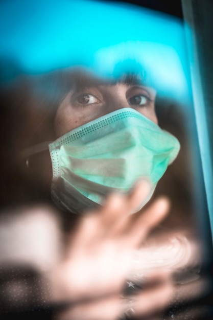 Una giovane donna caucasica che guarda fuori dalla finestra nella quarantena covid-19