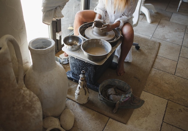 Una giovane donna ceramista siede dietro un tornio da vasaio Artigianato