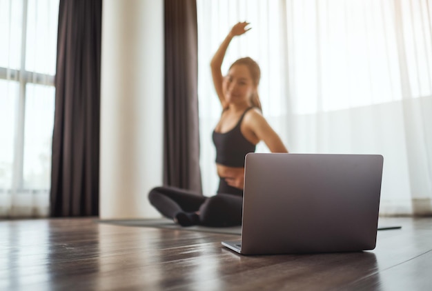 Una giovane donna che allunga le braccia mentre guarda i tutorial di allenamento online sul laptop a casa