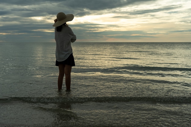 Una giovane donna che indossa un cappello è sola su una spiaggia sabbiosa deserta in riva al mare. I giovani turisti soli guardano l'orizzonte. Il concetto di solo, viaggio