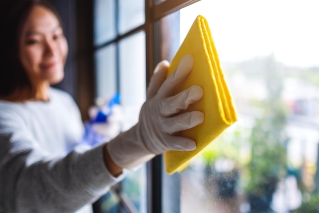 Una giovane donna che indossa un guanto protettivo che pulisce la finestra per il concetto di lavoro domestico