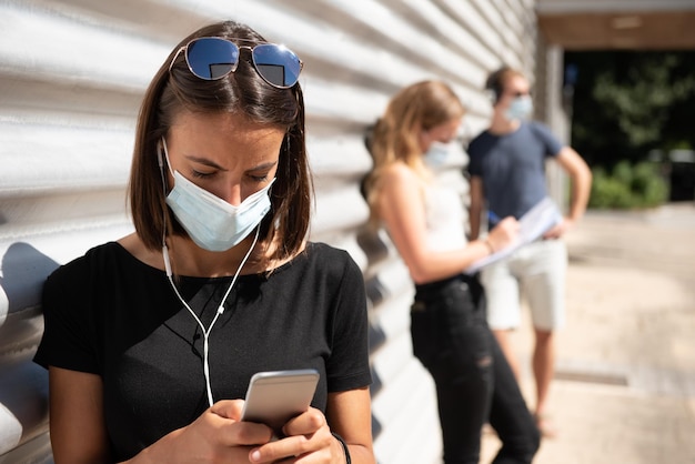 Una giovane donna che indossa una maschera e chiacchiera al cellulare in coda