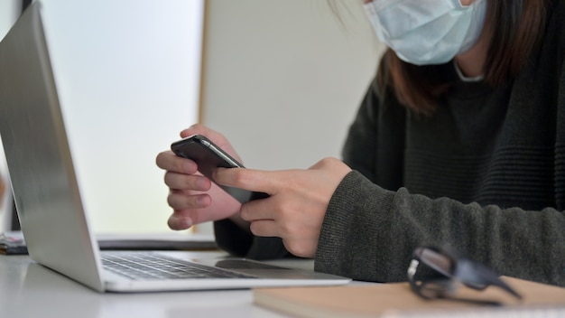 Una giovane donna che indossa una maschera utilizza uno smartphone durante la pausa studio.