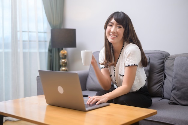 Una giovane donna che lavora con il suo laptop e prende una tazza di caffè, stile di vita e concetto di business