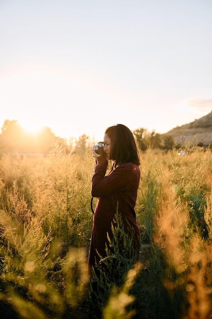 Una giovane donna che passeggia per la campagna con la sua macchina fotografica d'epoca al tramonto