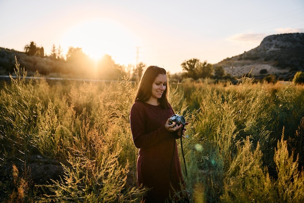 Una giovane donna che passeggia per la campagna con la sua macchina fotografica d'epoca al tramonto